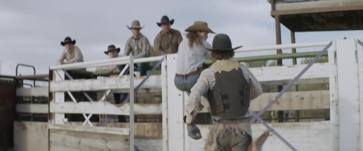 Cowboys run and scale a fence in an arena