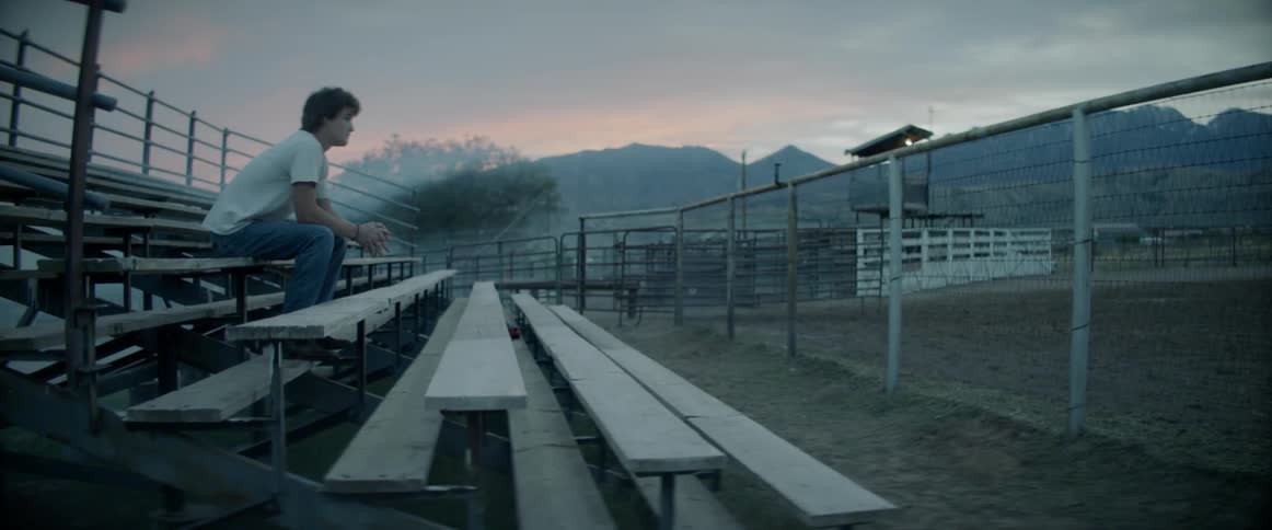 A young man sits in foggy bleachers at a bull riding arena