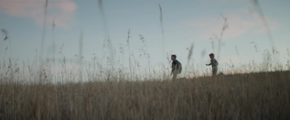 Two children run through the tall grass