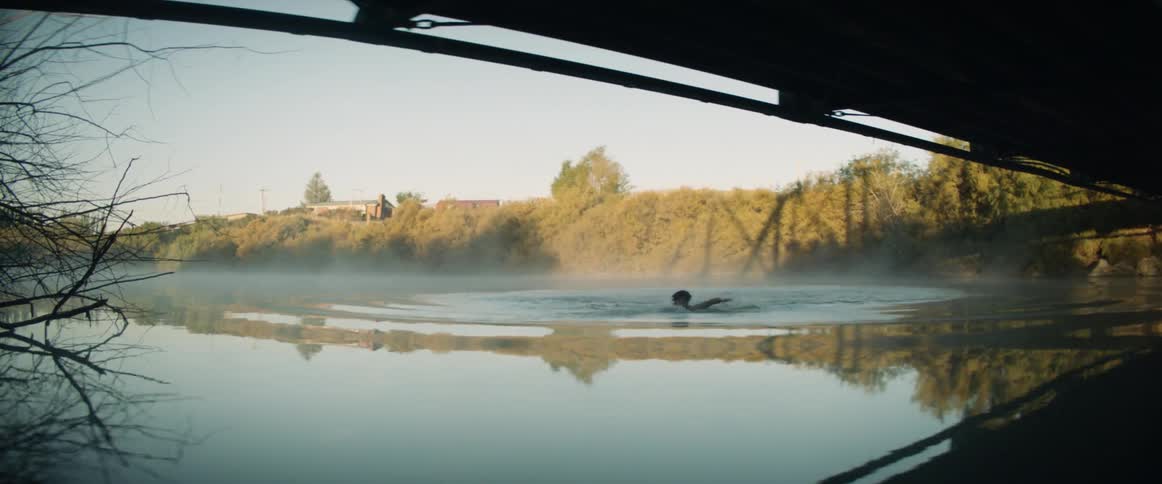 A person jumps and swims toward the bridge as another jumps in after
