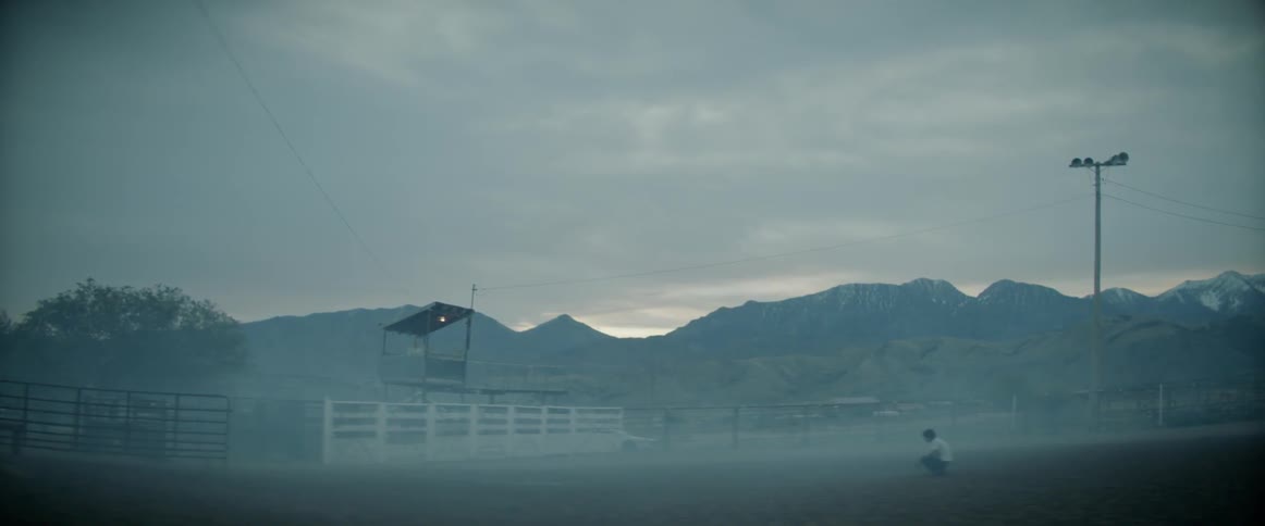 Man squats in the center of a rodeo ring at dawn