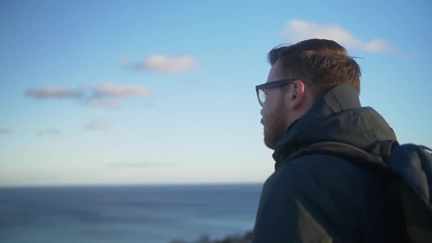 A young, bearded brunette man looking at the ocean on a chilly day