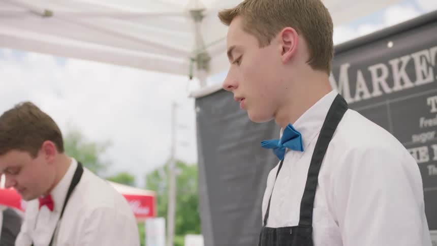 A teenager mixes a drink while working at an outdoor fair