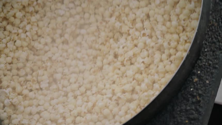 A man is stirring popcorn inside a large pot