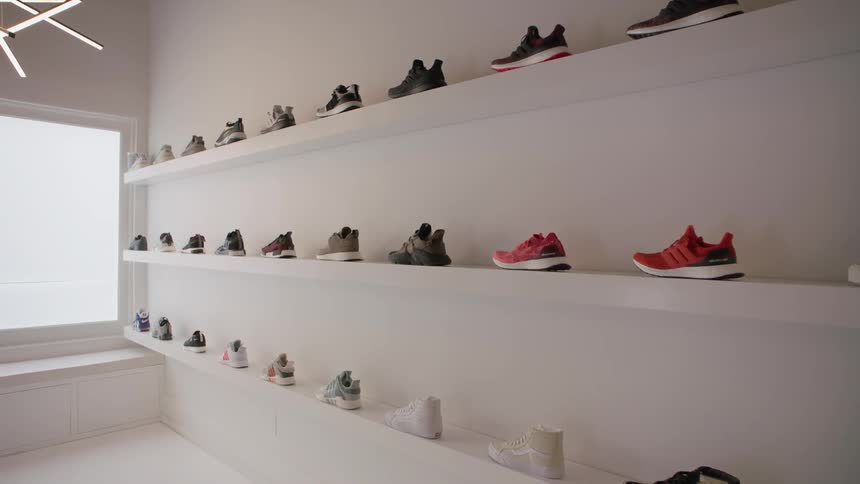 Sneakers are displayed on wall shelves in a white room