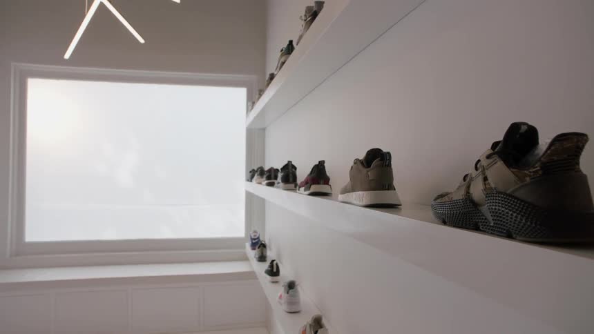 Shoes lined up on three shelves  in a white room with a window