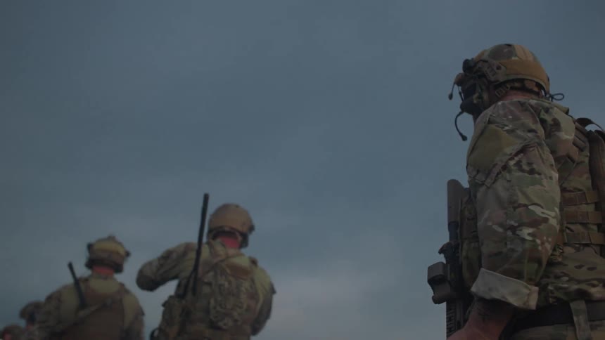 Soldiers stand on a rooftop and scan the area
