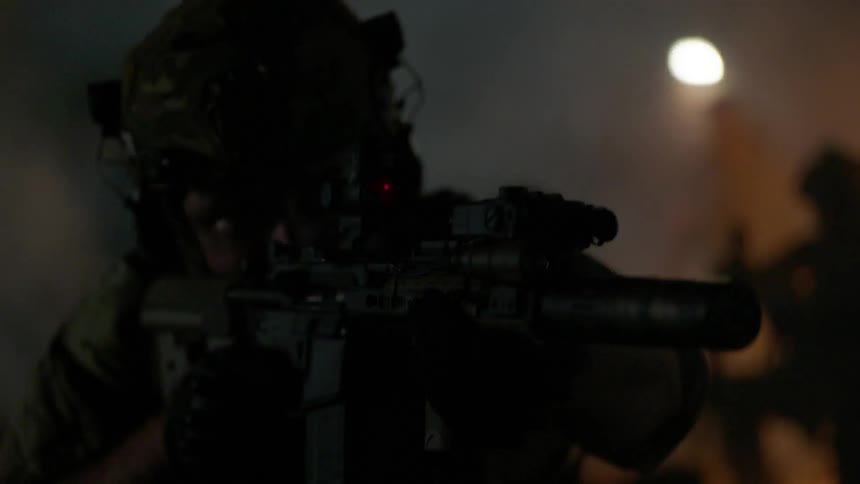 The soldiers aim their guns around a smokey field at night