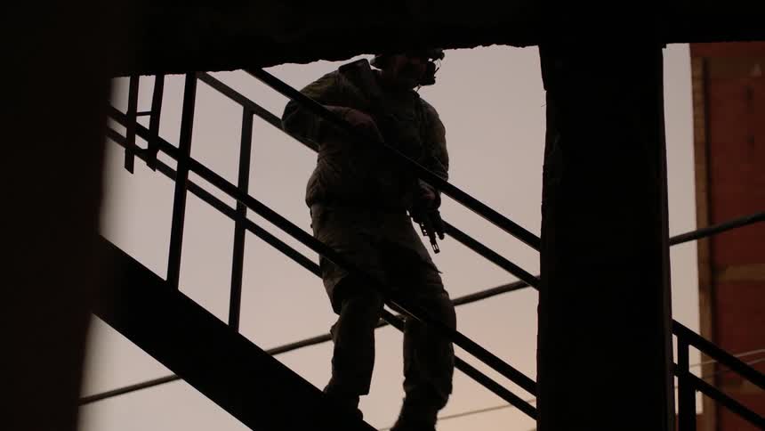 Man carrying a gun walks down a set of stairs