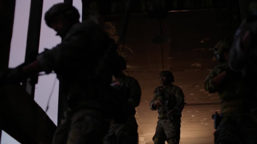 Uniformed men holding guns stand in a dim room