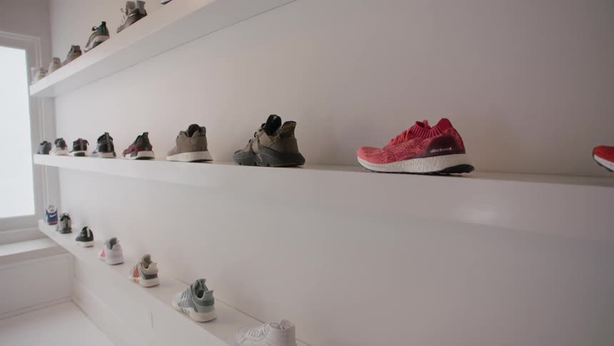 Sneakers are displayed on wall shelves in a white room