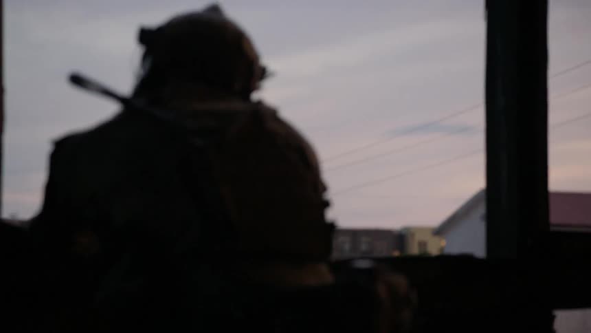 A soldier looks out from a tattered building window