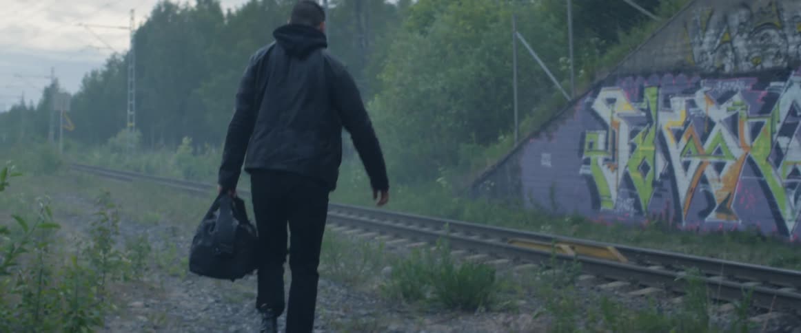A man walks across railroad tracks carrying a bag
