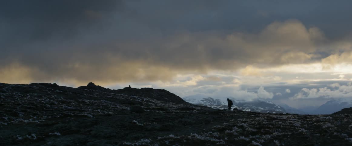 A backpacker hikes a rocky trail under dark clouds