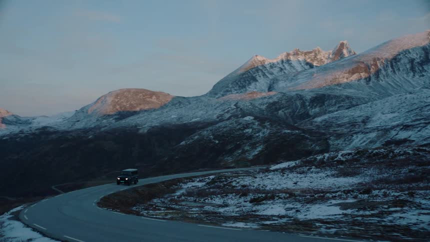 A vehicle drives through snowy mountains at sunset