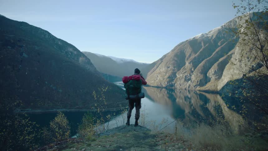 A hiker takes a photograph of a mountain lake