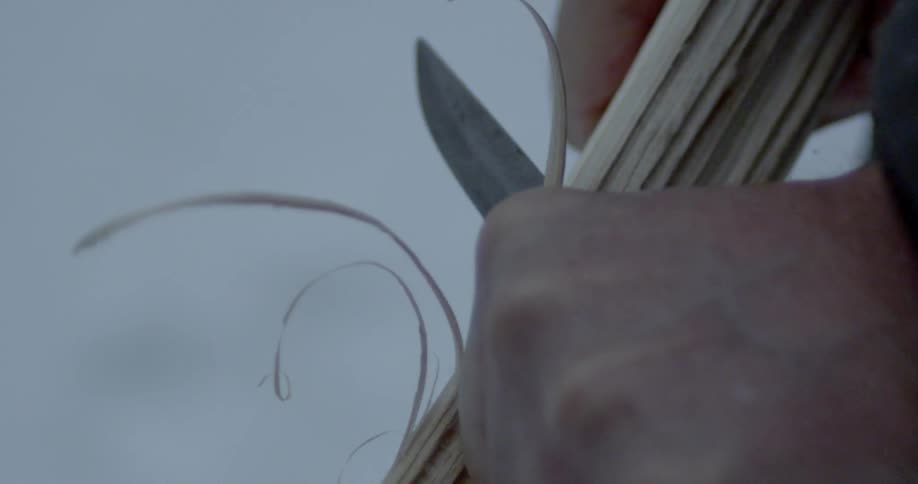 A man carves a piece of wood with a knife