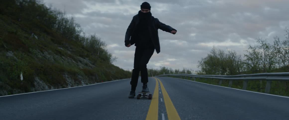 A man is skateboarding down the road on a windy day
