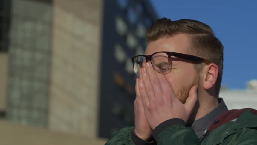 Man puts his hands over his mouth on a sunny day