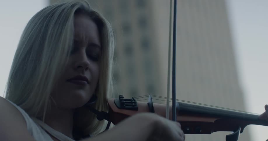 A woman plays a violin next to a skyscraper