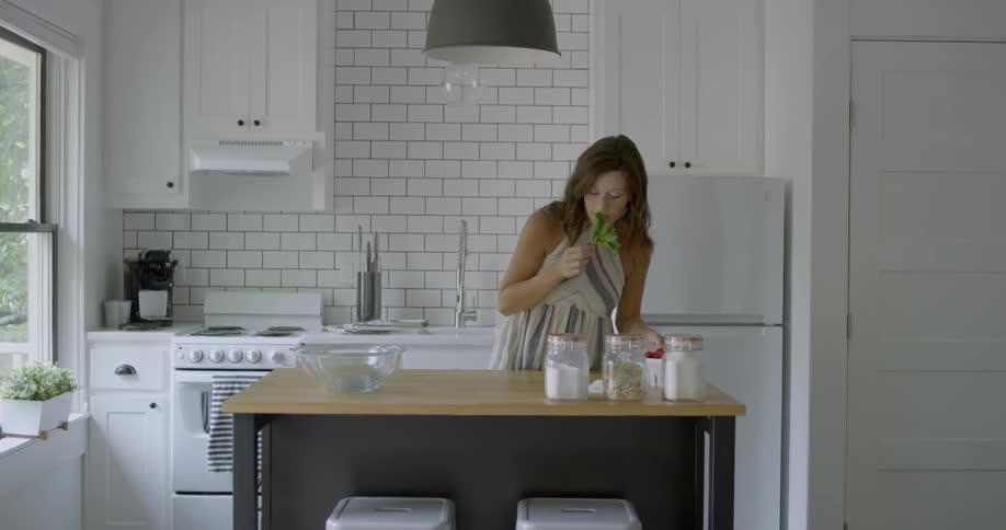 Woman walks into a kitchen with berries and grabs a glass bowl
