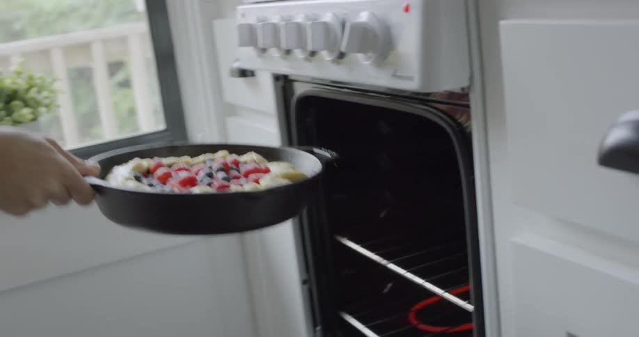 Woman in kitchen putting berry pie in skillet into the oven