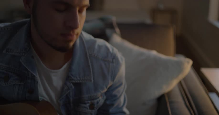 Man plays guitar while sitting on a couch