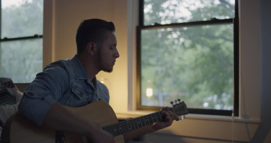 A man is playing guitar by the window