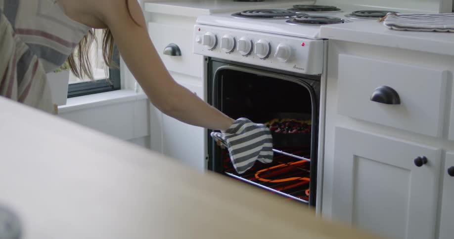 Woman opens an oven and pulls out a dessert