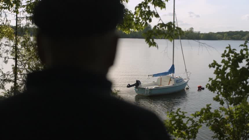 Man standing in the shade facing a boat docked in the water