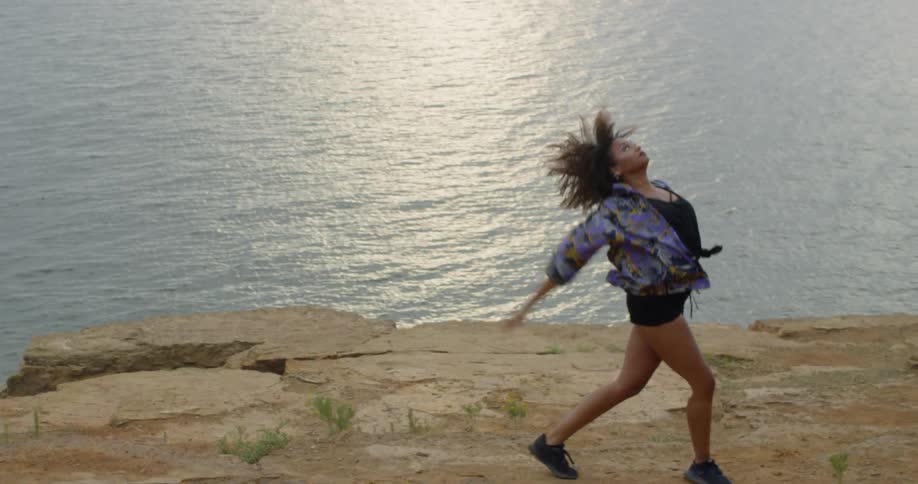 A woman dances next to a lake