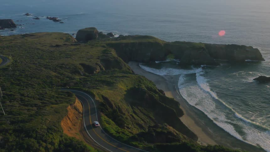 A vehicle travels down a coastal road by the ocean