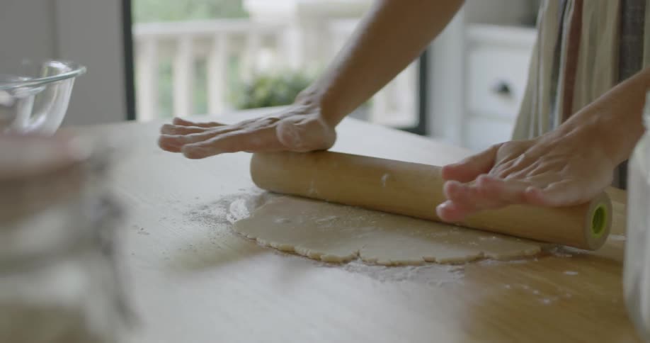 A woman sprinkles flour on dough and uses a rolling pin
