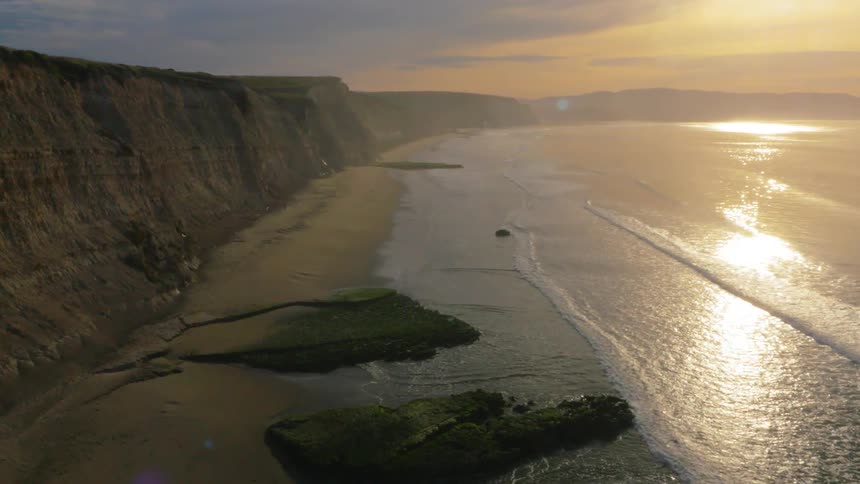 The waves crash against the short beach by the cliff