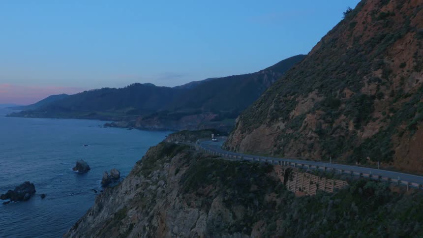 Car drives on a coastal mountain road at dusk