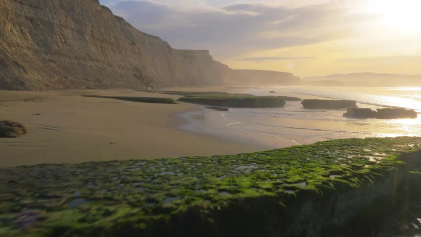 Waves flow towards the beach shore lined with tall cliffs