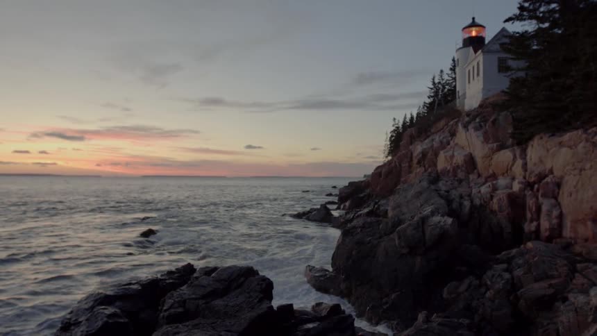 Waves Crash on Rocks Below a Lighthouse