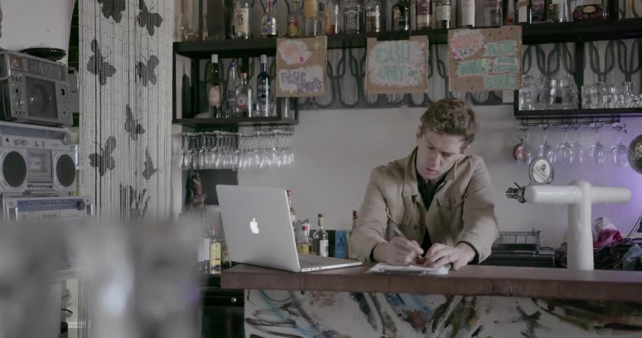 A man looks at his laptop then takes notes in a pad