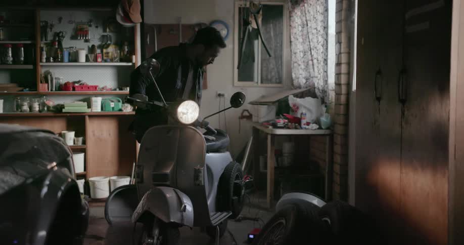A man in a garage turns a moped on then examines it