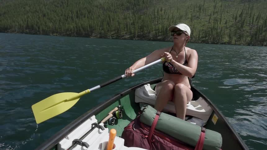 Woman paddling in canoe on forest lake on sunny day