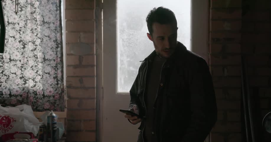 A man stands by the door and looks at his phone