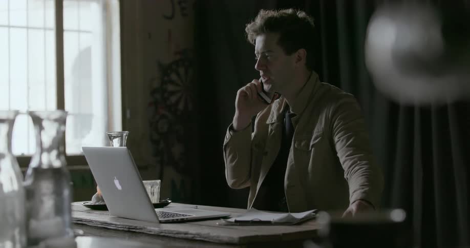 A man talks on his phone by a laptop