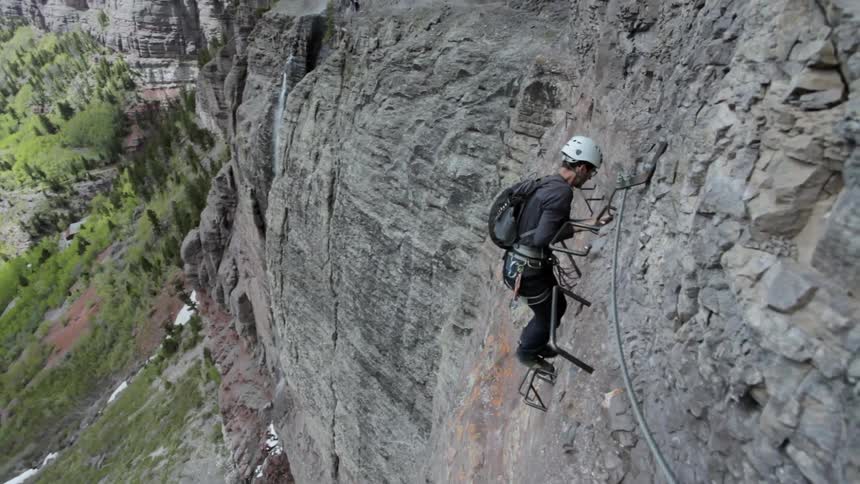 Man climbing up metal bars sticking out of mountain cliff