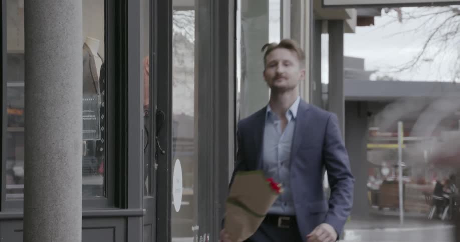 Man walking on city sidewalk is carrying bouquet of flowers