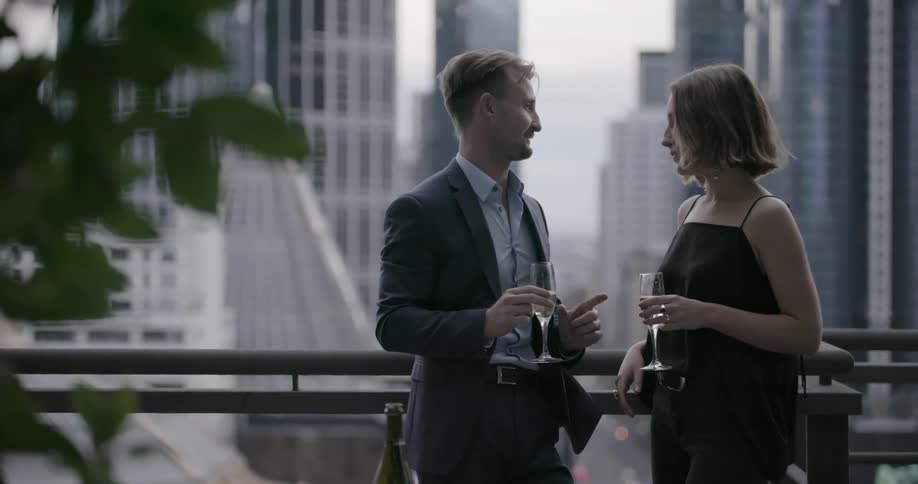 Man and woman drinking champagne and talking on balcony in city