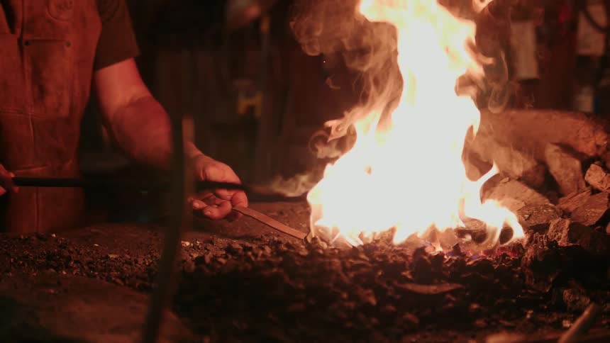A blacksmith stirs the fire making it blaze