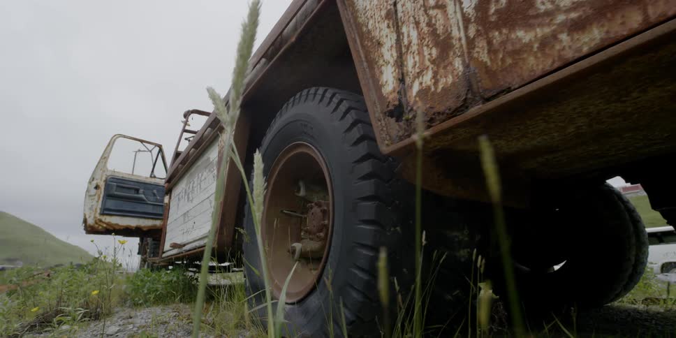 An old truck is sitting deteriorating in a field during the day