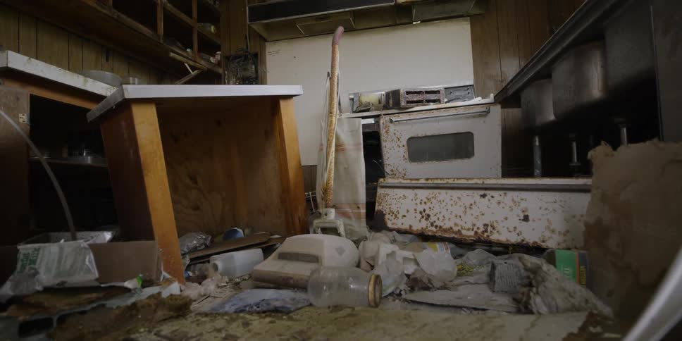 Debris and destroyed cabinets and appliances in a kitchen