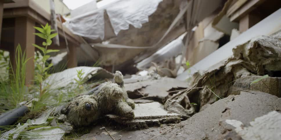 A stuffed teddy bear lays in the wreckage of a house