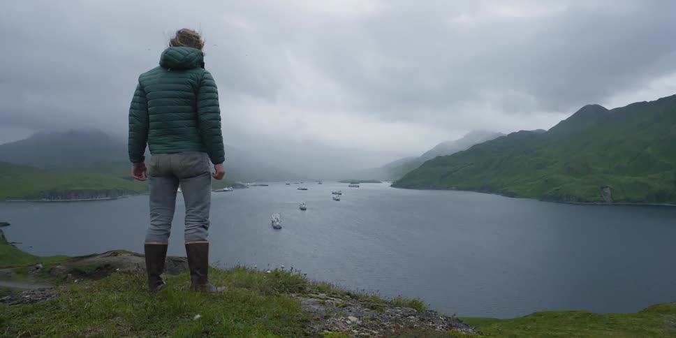 Wind ruffles a man's clothes on a cliff over sea